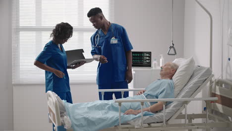 Two-African-American-doctors-a-man-and-a-woman-examine-and-talk-to-an-elderly-patient-lying-on-a-bed-in-a-hospital